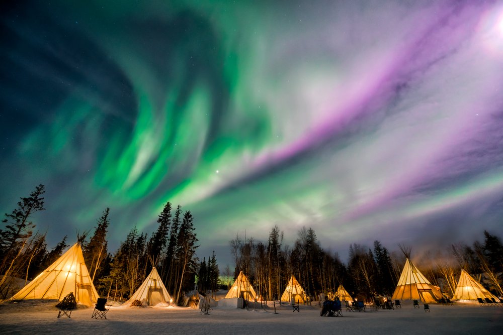 Heated canvas teepees standing apart on a snow-covered lakeshore at night.