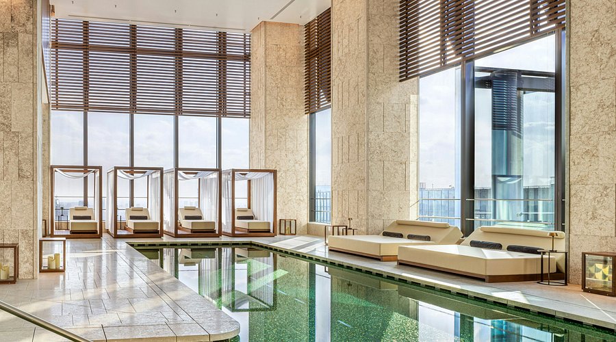A high interior lounge in a modern tower with glass walls looking over a city at dusk.